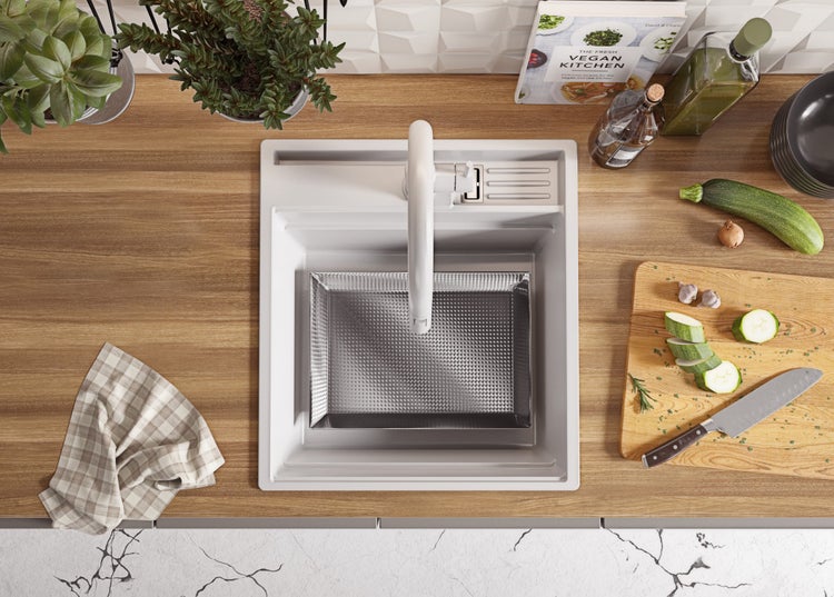 Aufsicht auf eine Küchenspüle mit Armatur, Abtropfsieb, Schneidebrett mit Gemüsezucchini, Messer und Kochbuch