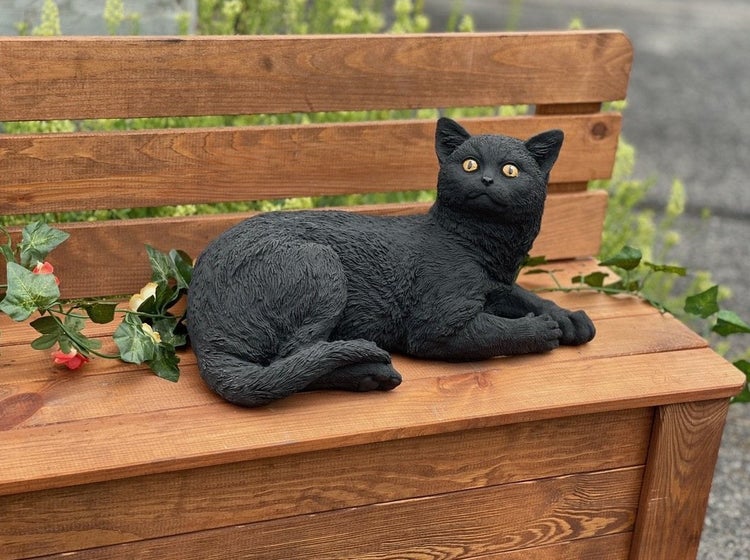 Gartenfigur Katze liegend aus wetterfestem Material zur Dekoration auf einer Holzbank.