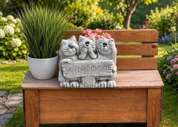 Gartendekoration Katzenfigur mit Willkommen Schild aus Steinoptik auf einer Holzbank im Garten platziert.