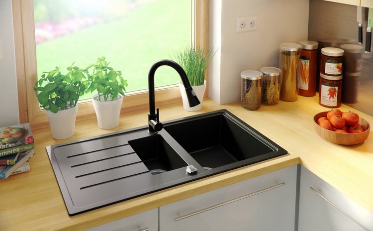 Schwarze Küchenspüle mit Abtropffläche und Wasserhahn in einer hellen Küche.