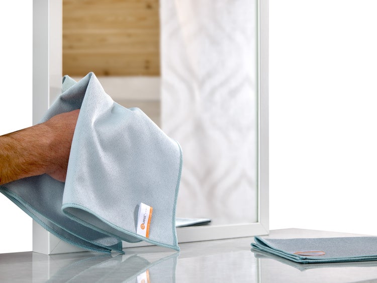 Ein Mann wischt einen Spiegel mit einem blauen Mikrofasertuch von Quest Home