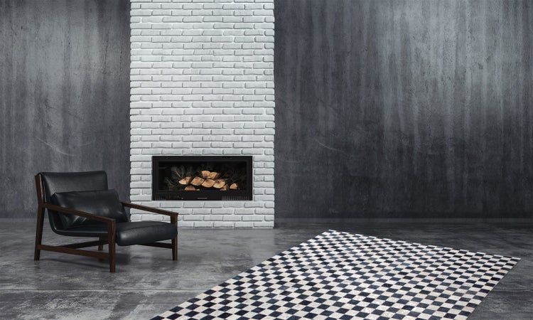 Moderner Raum im Industrie-Stil mit Sichtbetonwänden, weißem Backsteinkamin, schwarzem Ledersessel und kariertem Teppich auf Betonboden.
