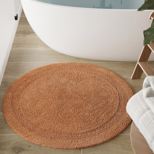 Runder Badteppich mit strukturierter Oberfläche vor einer weißen Badewanne auf Holzboden im Badezimmer.