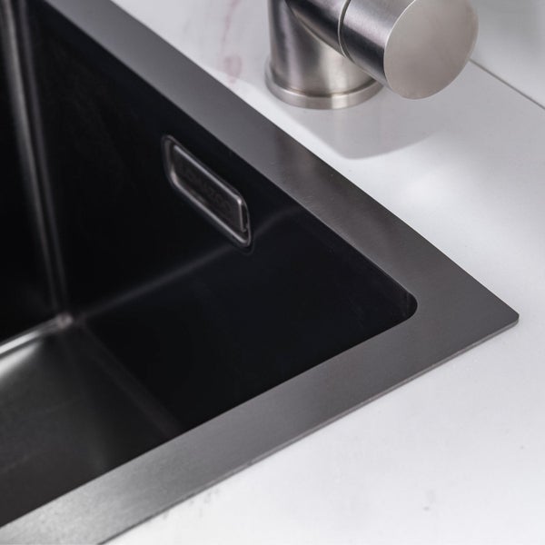 Edelstahlspüle mit integriertem Überlauf in einer weißen Arbeitsplatte mit Wasserhahn.
