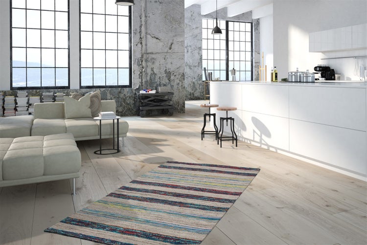 Modernes Loft im Industriestil mit hellem Holzboden, gestreiftem Teppich, hellem Modulsofa, großen Fenstern und weißer Kücheninsel.