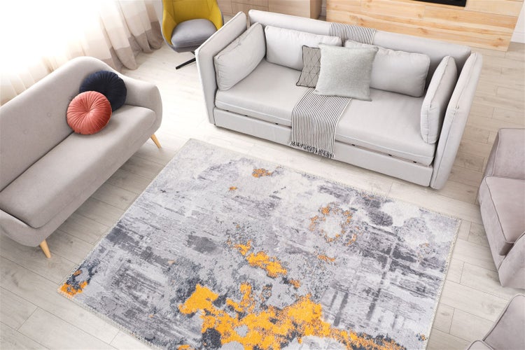 Modernes Wohnzimmer mit abstraktem Teppich in Grau und Gelb, hellgrauen Sofas und hellem Bodenbelag.