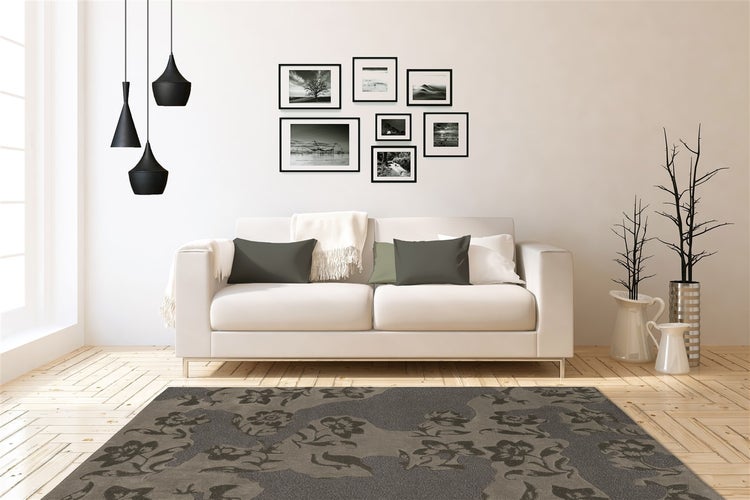 Modernes Wohnzimmer mit hellem Sofa, dunklem Blumenteppich und schwarzen Bilderrahmen. Drei schwarze Pendelleuchten und Vasen mit Zweigen auf hellem Holzboden.