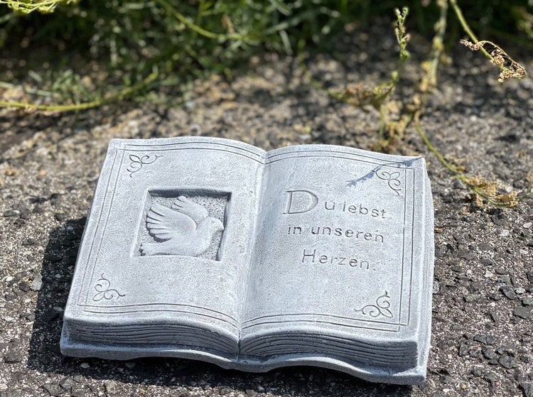 Grabschmuck in Form eines aufgeschlagenen Buches mit eingravierter Taube und dem Text Du lebst in unseren Herzen aus wetterfestem Material.