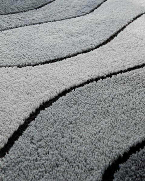 Nahaufnahme eines Hochflor-Teppichs mit Wellenmuster in Grau und Schwarz.