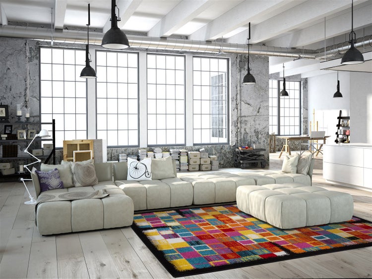 Modernes Wohnzimmer im Loft-Stil mit hellem Modulsofa, buntem Teppich und großen Fenstern vor einer Wand in Betonoptik.