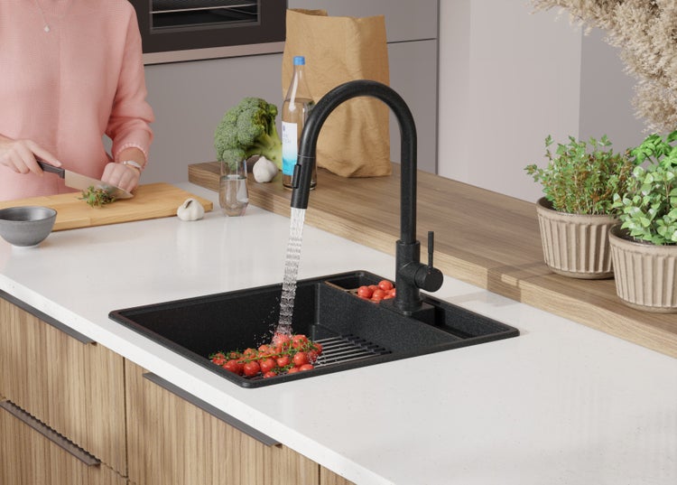Küchenszene mit schwarzer Spüle, Armatur und Person beim Gemüseschneiden