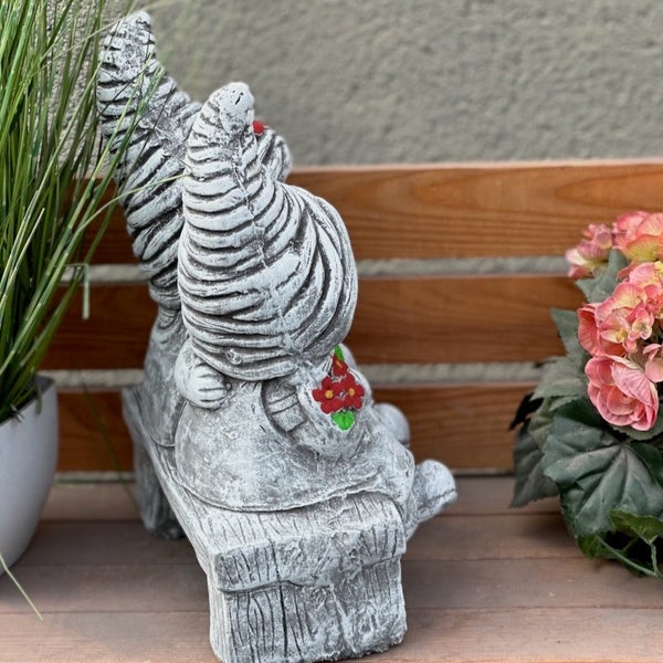 Zwei Gartenzwerge aus Stein auf einer Bank sitzend, dekorative Gartenfigur.