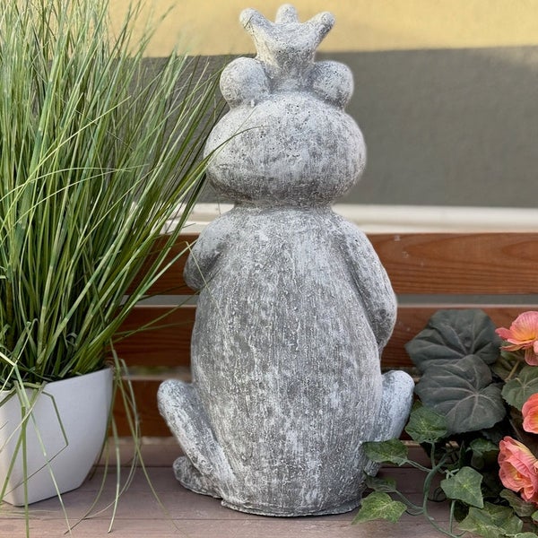 Gartenfigur Frosch mit Krone in Steinoptik, Ansicht von hinten, platziert auf einer Holzbank neben Pflanzen.