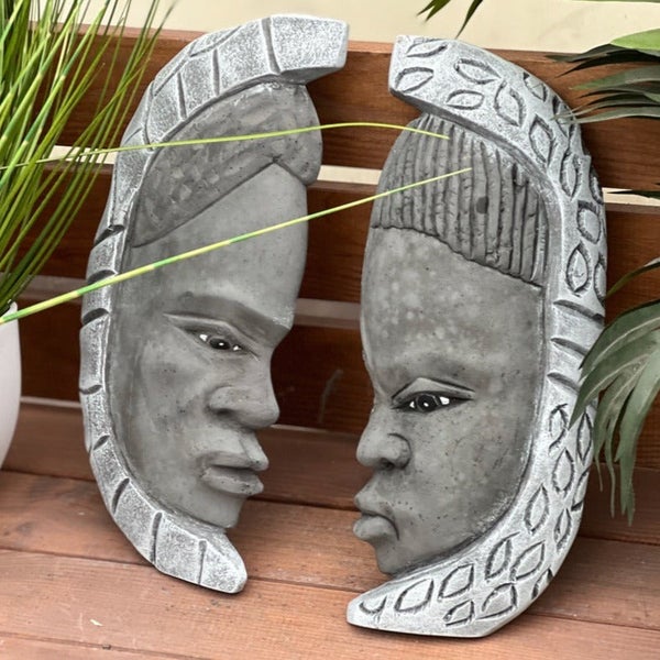 Zwei dekorative Wandmasken aus Beton mit ethnischen Gesichtern und strukturierter Umrandung für die Wandgestaltung.