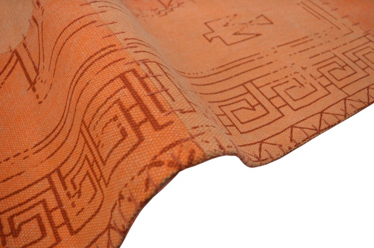 Nahaufnahme eines orangefarbenen gewebten Teppichs mit Mäandermuster und geometrischen Ornamenten.