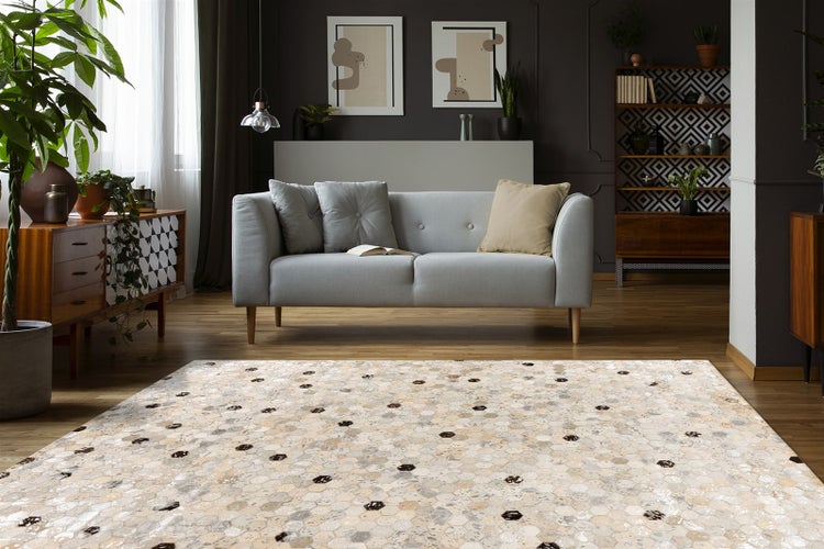 Heller Wohnraum mit Teppich mit sechseckigem Muster in Beige und Grau auf Holzfußboden, dazu graues Sofa und Holzmöbel in modernem Design.