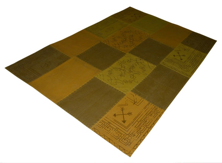 Rechteckiger Teppich im Patchwork-Design mit geometrischen Mustern und Symbolen in Braun, Ocker und Olivgrün.