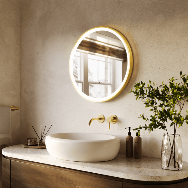 Modernes Badezimmer mit rundem LED Spiegel, Aufsatzwaschbecken und goldfarbener Unterputzarmatur auf einem Waschtisch mit Steinplatte.