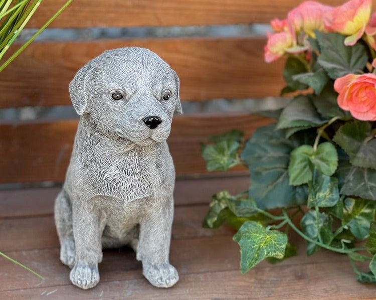 Gartenfigur aus Steinguss in Form eines sitzenden Welpen auf einer Holzbank.