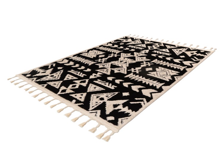 Rechteckiger Teppich mit geometrischem Ethno-Muster in Schwarz und Weiß sowie dekorativen Fransen an den Schmalseiten.