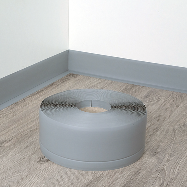 Eine Rolle PVC Sockelleiste zur Wandgestaltung auf einem Holzoptikboden vor einer bereits installierten Fußleiste.