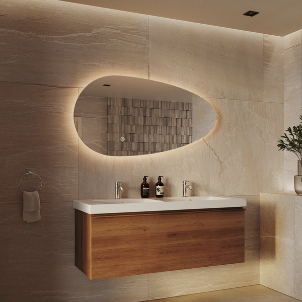 Modernes Badezimmer mit organisch geformtem LED Wandspiegel über einem Doppelwaschtisch mit Holzunterschrank vor einer steinernen Wandverkleidung.