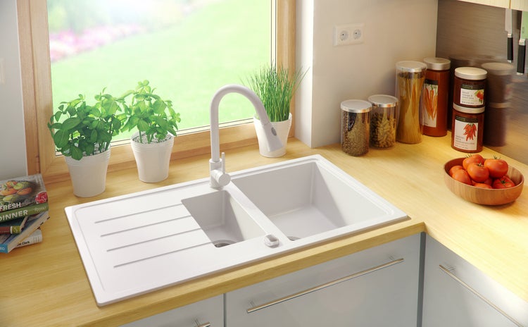 Küchenszene mit Spüle, Armatur, Kräutern und Kochzutaten auf einer hellen Arbeitsfläche