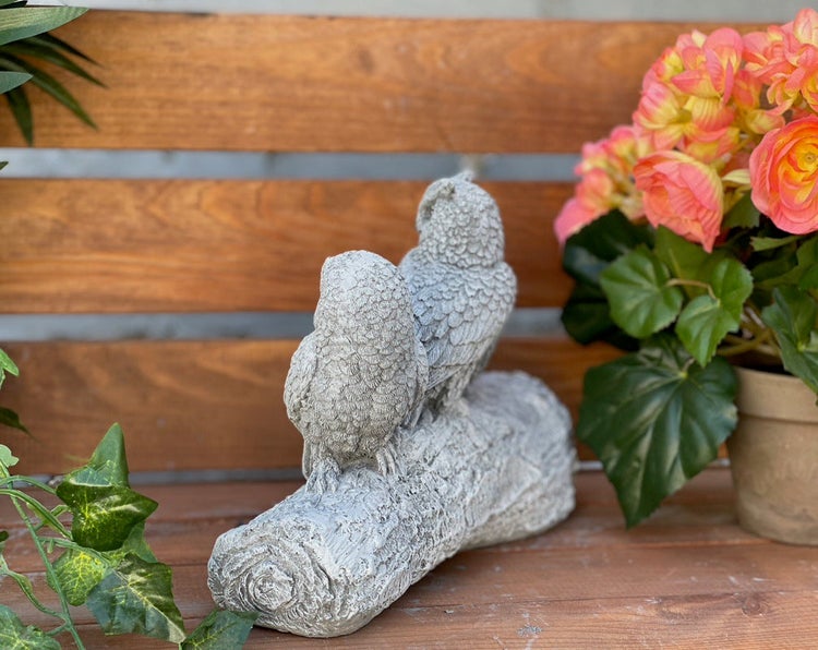 Zwei Eulen als Gartenfigur aus Kunststein auf einem Baumstamm sitzend zur Dekoration im Garten oder auf der Terrasse.