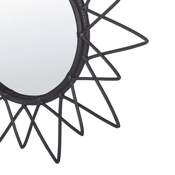 Detailansicht eines runden Wandspiegels mit schwarzem Rattanrahmen in Sonnenform.