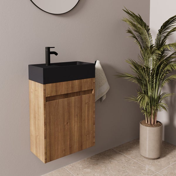Ein wandhängender Waschbeckenunterschrank aus Holzoptik mit dunklem Waschbecken und Armatur in einem modern eingerichteten Badezimmer.