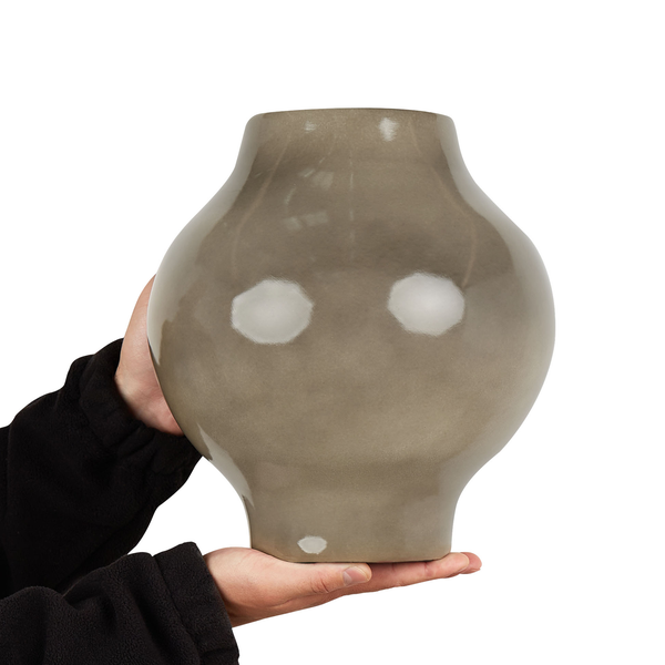 Eine Person hält eine bauchige Keramikvase mit glatter Oberfläche in den Händen.