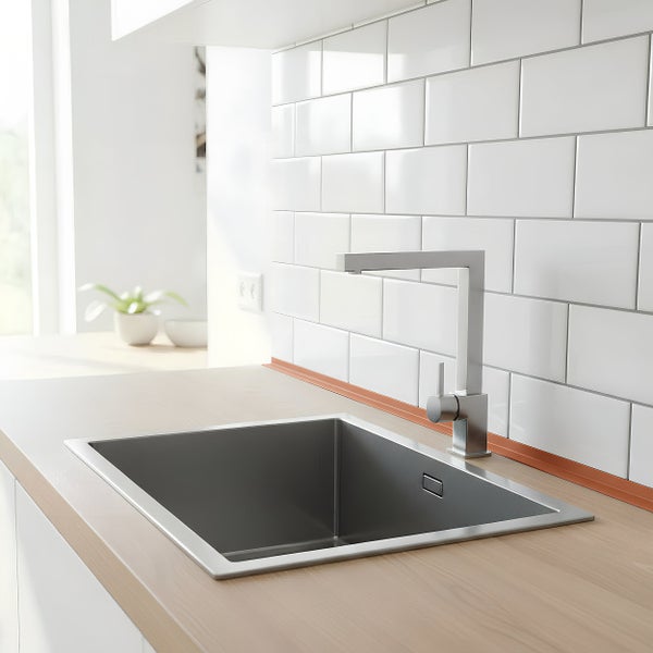Moderne Küchenspüle aus Edelstahl mit quadratischer Armatur eingebaut in eine helle Arbeitsplatte vor einem gefliesten Küchenrückwandbereich.