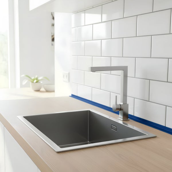 Moderne Edelstahl Küchenspüle mit quadratischer Armatur eingelassen in eine helle Holzarbeitsplatte vor einem Fliesenrückspiegel in der Küche.
