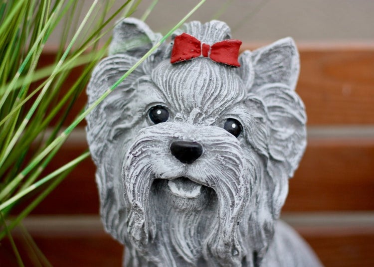 Gartenfigur Hund Yorkshire Terrier aus Steinguss mit einer roten Schleife auf dem Kopf, Nahaufnahme.