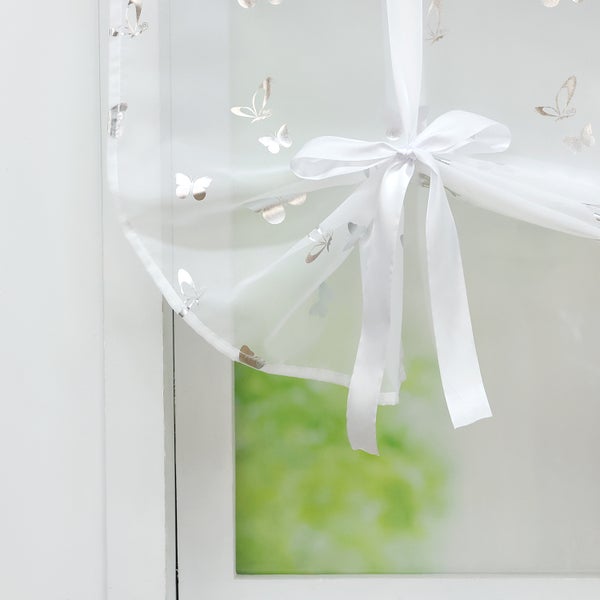 Gardine mit Schmetterlingsmuster und Bindeband gerafft vor Fenster