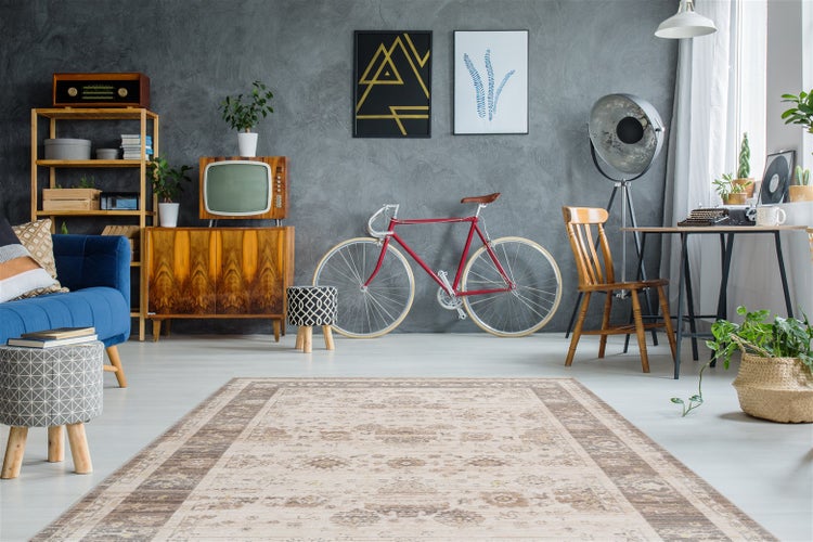Orientalischer Vintage-Teppich in Beige und Braun in einem hellen Retro-Wohnzimmer mit Holzmöbeln, Fahrrad und Zimmerpflanzen.