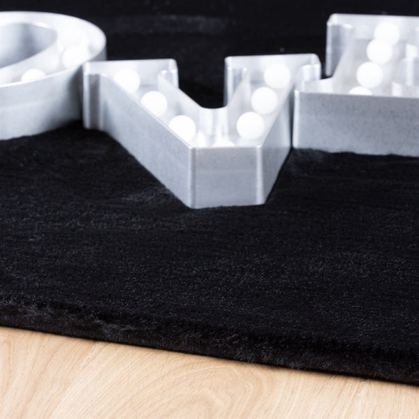 Schwarzer Hochflor-Teppich aus Kunstfell mit dekorativen Leuchtbuchstaben auf hellem Holzboden.