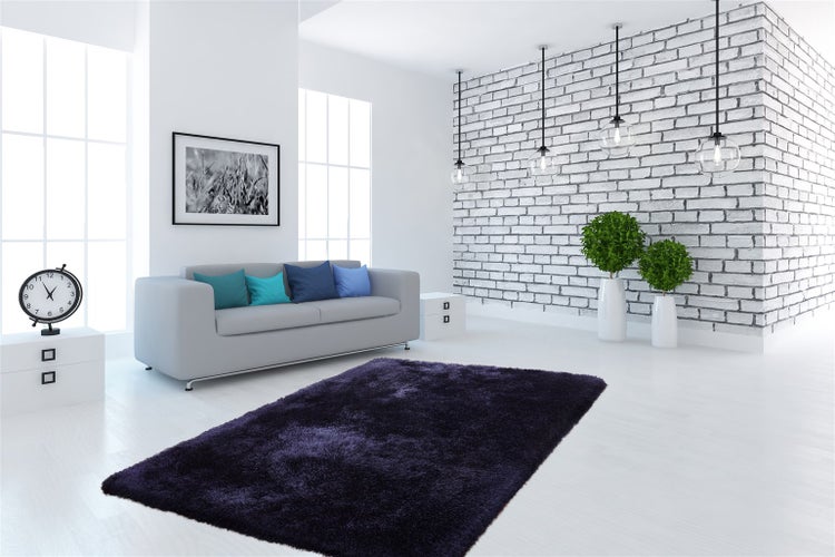 Modernes Wohnzimmer mit grauem Sofa, dunkelviolettem Hochflor-Teppich, weißer Ziegelwand und gläsernen Pendelleuchten.