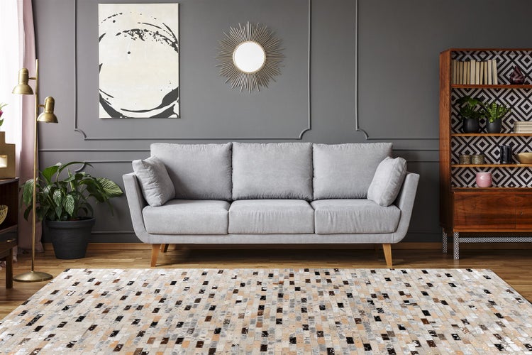 Modernes Wohnzimmer mit Stoffsofa, Teppich mit geometrischem Muster, Holzregal, Sonnenspiegel und Stehlampe.