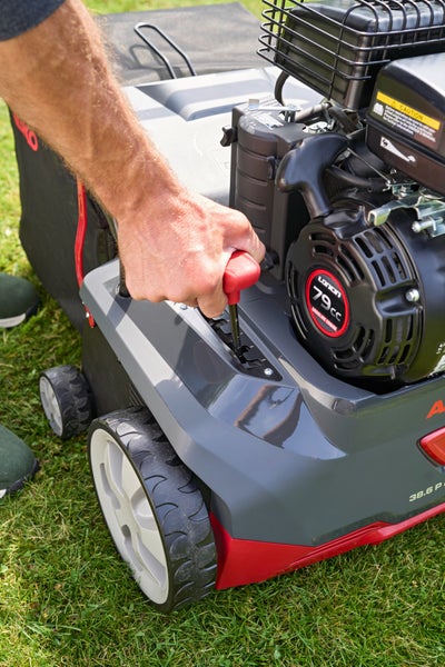 Eine Hand bedient den Hebel zur Einstellung der Arbeitstiefe an einem Benzin-Vertikutierer mit Loncin Motor.