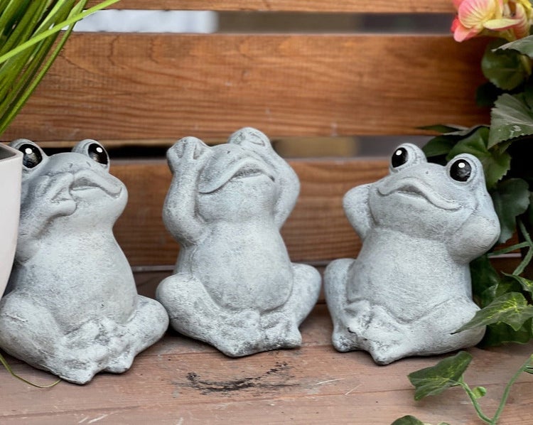 Drei sitzende Froschfiguren aus Beton in einer Dekoration