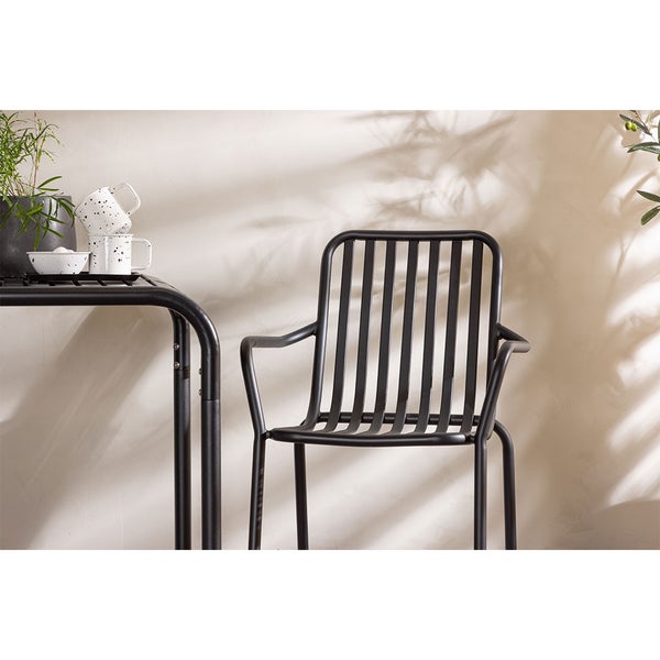 Schwarzer Metallstuhl neben einem Tisch mit Geschirr und einer Pflanze