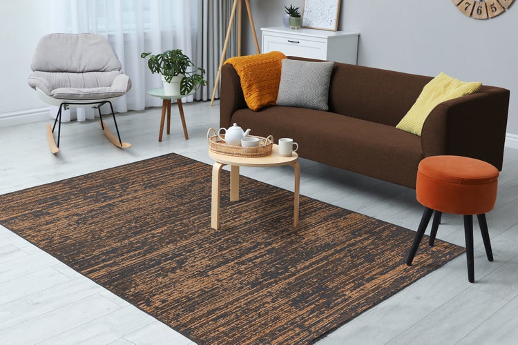 Modernes, helles Wohnzimmer mit braunem Sofa, gemustertem Teppich in Brauntönen, einem Schaukelstuhl und einem runden Couchtisch aus Holz.