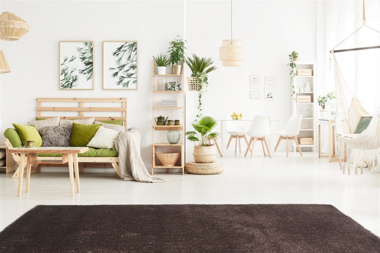 Helles Wohnzimmer mit Holzmöbeln, dunkelbraunem Teppich, grünen Kissen, Essbereich und Pflanzen in einem natürlichen Stil.