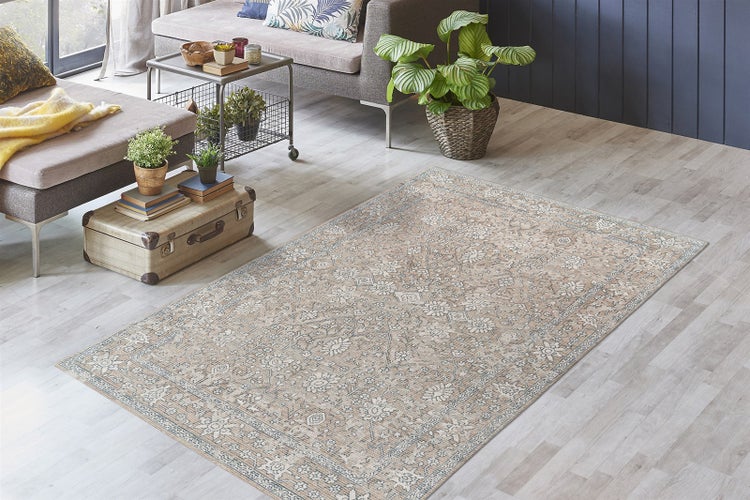 Beiger Teppich mit Orient-Muster im Vintage-Stil in einem hellen Wohnzimmer auf hellem Holzboden mit Sofa und Zimmerpflanzen.