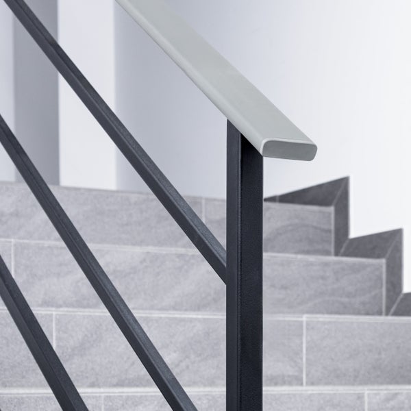 Modernes Treppengeländer aus Metall mit schwarzem Pfosten und Querstreben sowie einem hellgrauen Handlauf an einer gefliesten Treppe.
