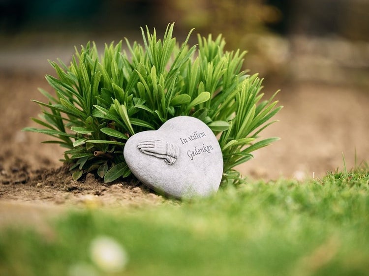 Herzförmiger Gedenkstein aus Stein mit der Inschrift In stillem Gedenken und einem Relief betender Hände platziert im Garten.