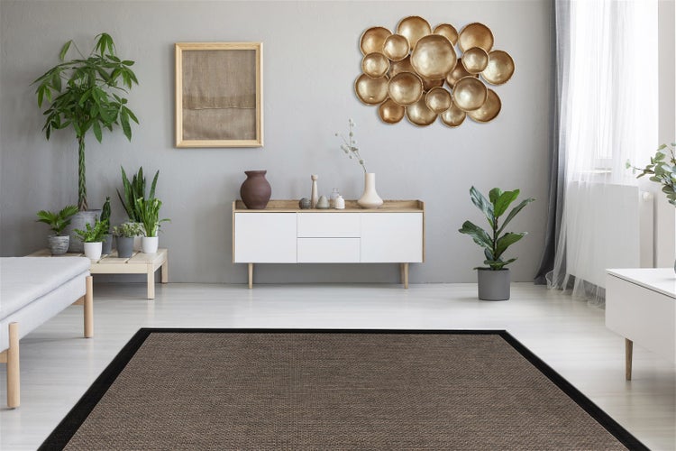 Moderner Wohnraum mit braunem Webteppich, schwarzer Bordüre, weißem Sideboard, goldener Wanddekoration und Zimmerpflanzen.