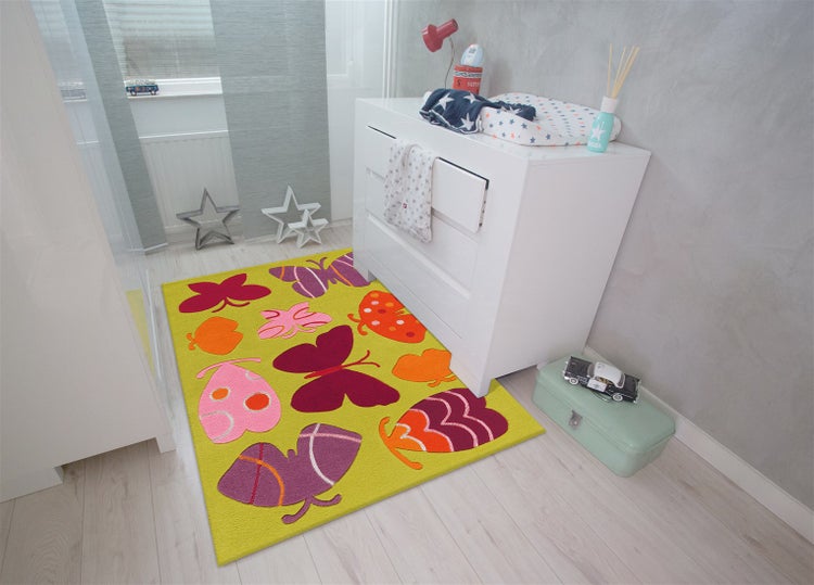 Hell eingerichtetes Kinderzimmer mit einem bunten Schmetterlingsteppich, einer weißen Kommode und hellem Bodenbelag.