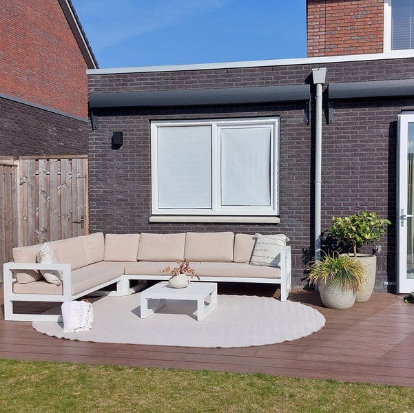 Gartenszene mit Ecksofa, Couchtisch und rundem Teppich auf einer Holzterrasse